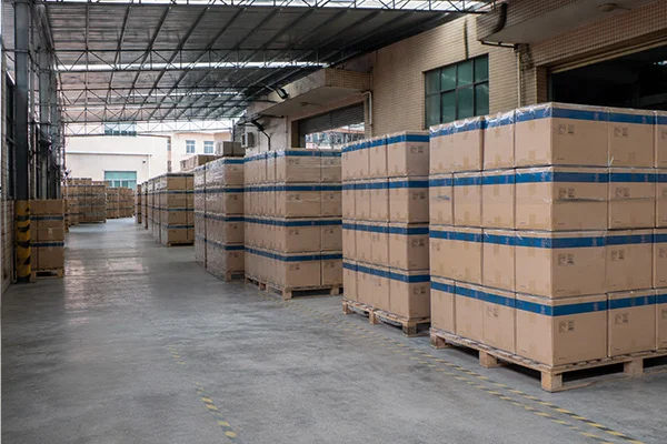 Industrial warehouse with piles of cardboard boxes stacked on wooden pallets, arranged neatly in rows under a metal roof.